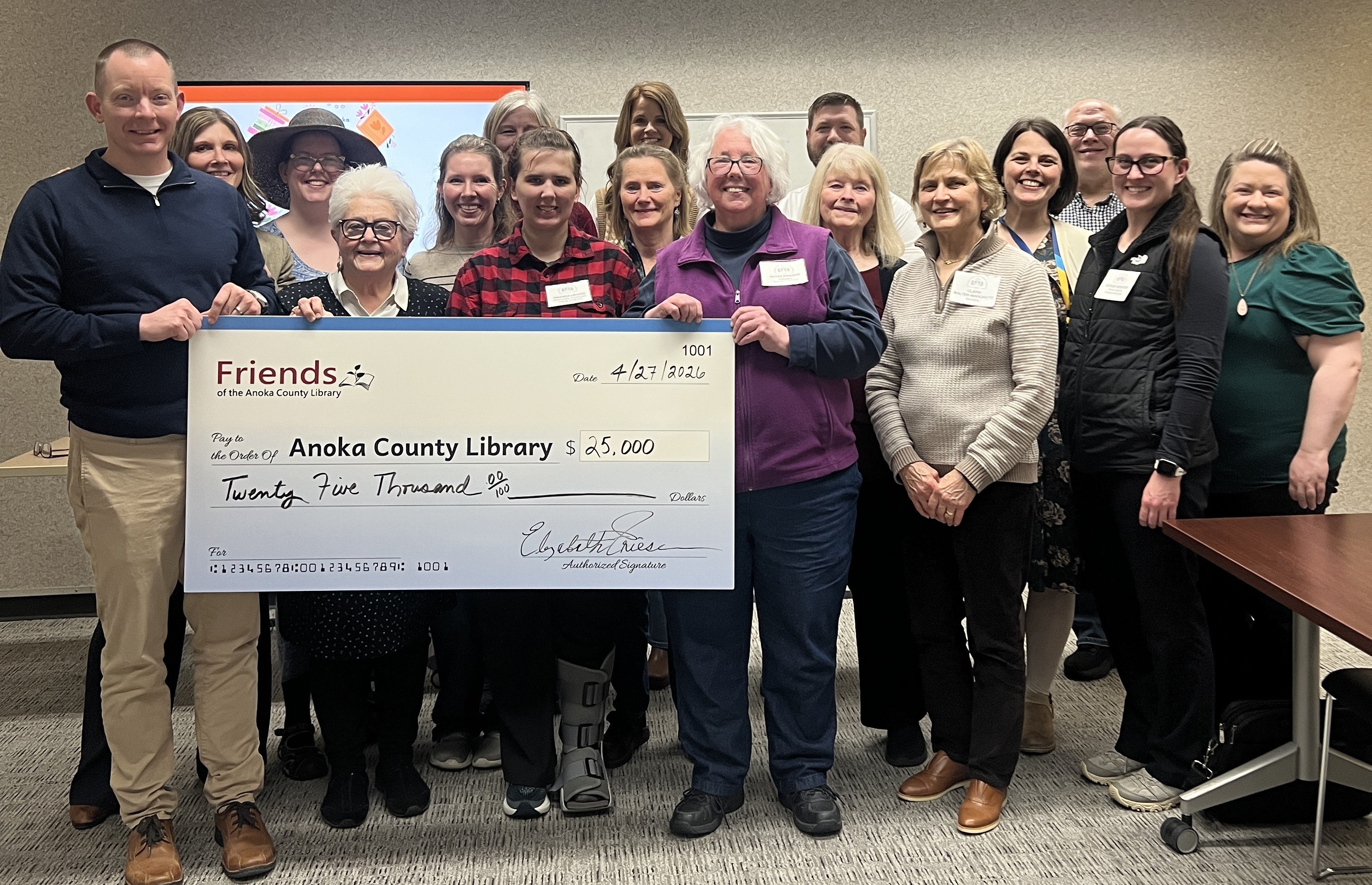 A larger group photo of Friends board members together with Anoka County Library staff and the Library Advisory Board, gathered around the $25,000 check.