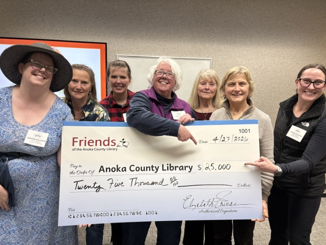 Friends of the Anoka County Library board members holding an oversized $25,000 check made out to the Anoka County Library, dated 4/27/2026.