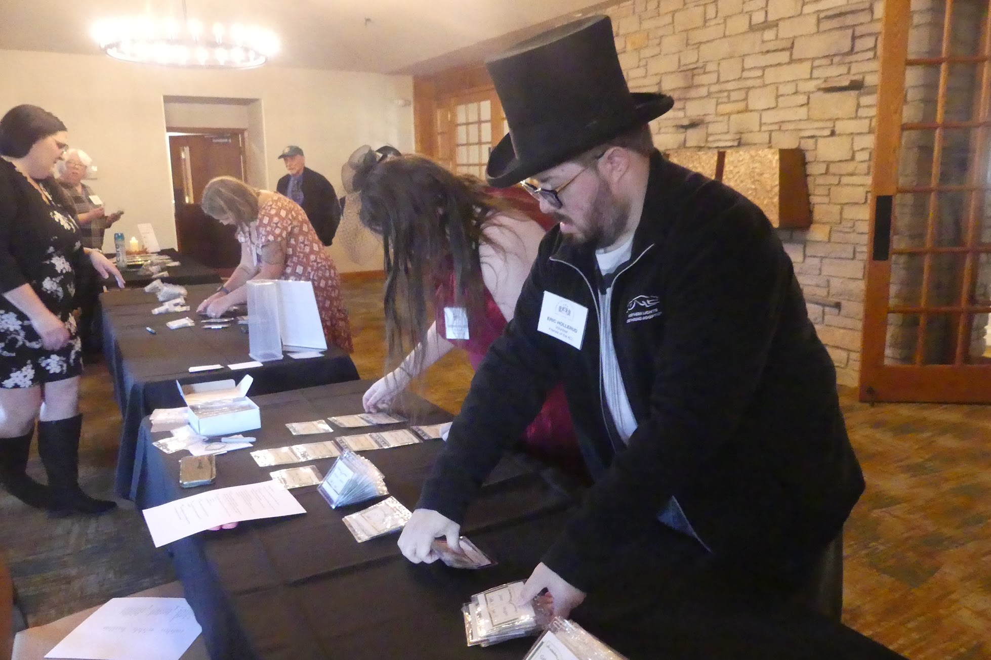 Several people stand on either side of registration tables draped in black, arranging name tags for the 2025 gala: An Evening with Friends and Authors. They are dressed up for the occasion.